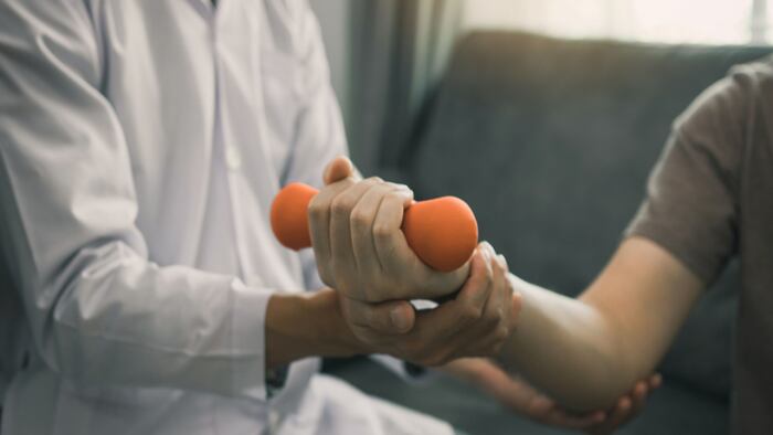 Young male physiotherapist helping patient with lifting dumbbells exercises in office