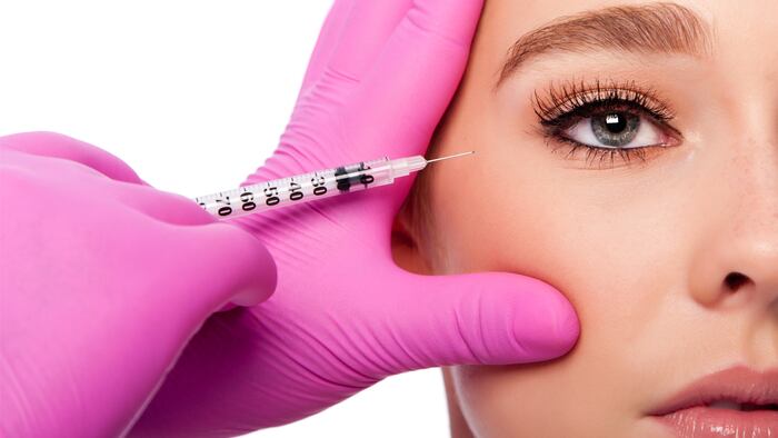 Beautiful face crows feet collagen filler injection Cosmetic skincare spa beauty treatment with pink gloves by eye, on white. - Image