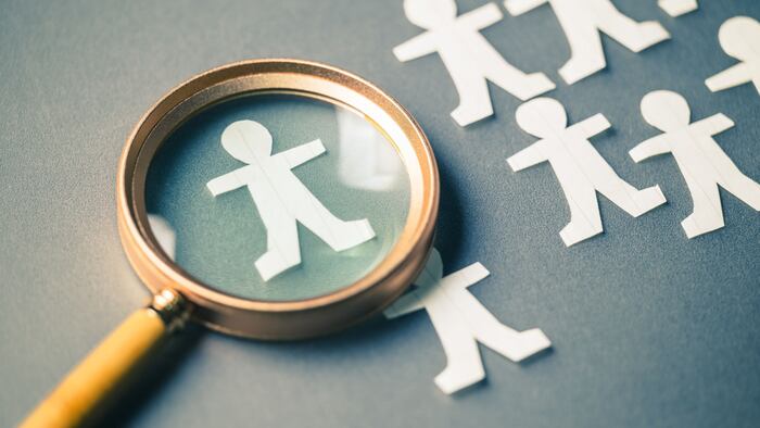Magnifying glass placed on the table with group of paper human dolls, and only one in the focus