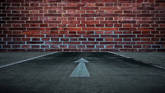 white arrow on road pointing towards dead-end brick wall
