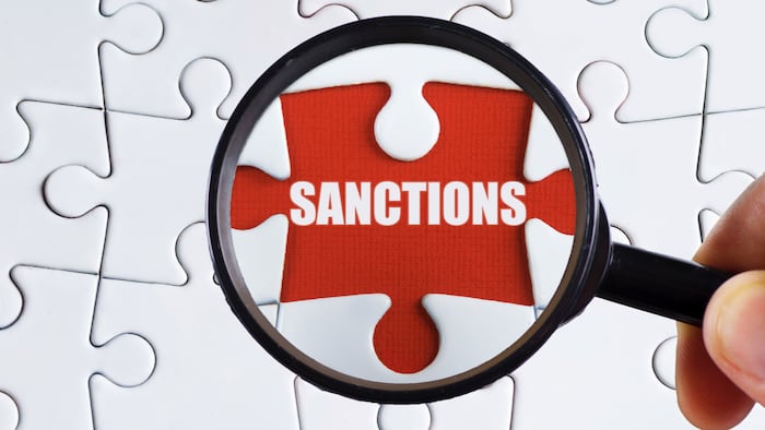Puzzle pieces with one removed to reveal the word 'SANCTIONS' under a magnifying glass