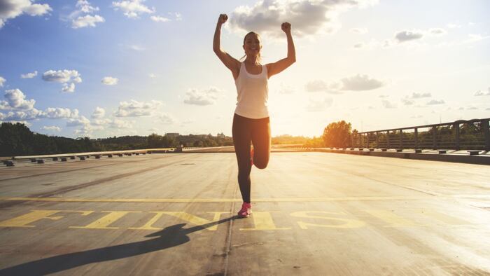 Winner as style of life. Horizontal shot of young beautiful woman in sports clothing keeping arms raised and smiling while passing finish line during jogging.