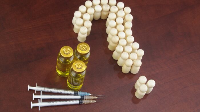 Many people shaped as question mark, vaccine bottles and syringes on wooden background. Questions about vaccination concept.