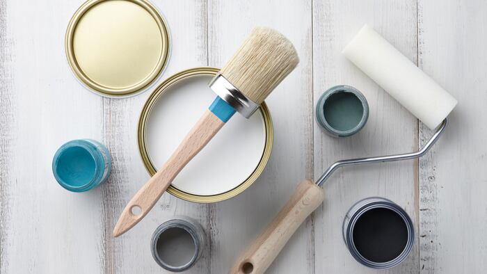 Paint brush, sponge roller, paints, waxes and other painting or decorating supplies on white wooden planks, top view