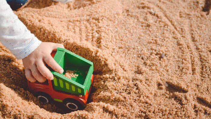 Child playing with his truck toy on a sunny summer day sandy background.