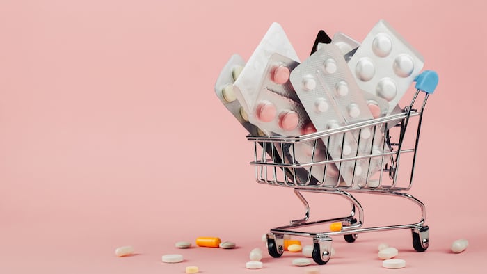 Shopping cart loaded with pills on pink background. The concept of medicine and the sale of drugs. Copy space. - Image