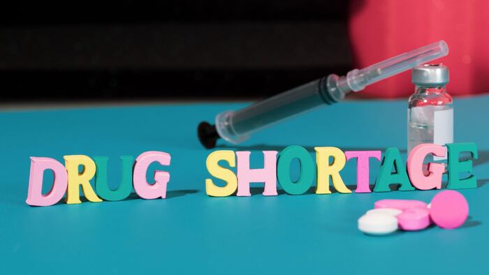 Letters spelling out 'drug shortage', pills and a syringe