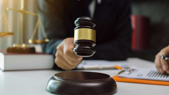 A hand holding a gavel over a block, with scales of justice in the background