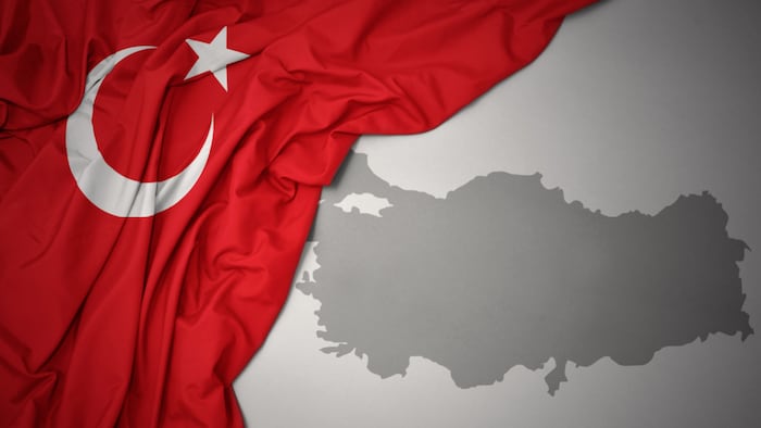 waving colorful national flag of turkey on a gray map background
