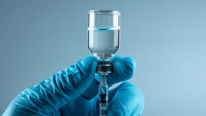 Gloved hand holding a vial and syringe