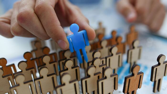 A businessman in blue shirt is holding a magnifying glass in his hand, is searching for personnel or people. Detective looking for missing person crowd of miniature figures choosing most suitable one - Image