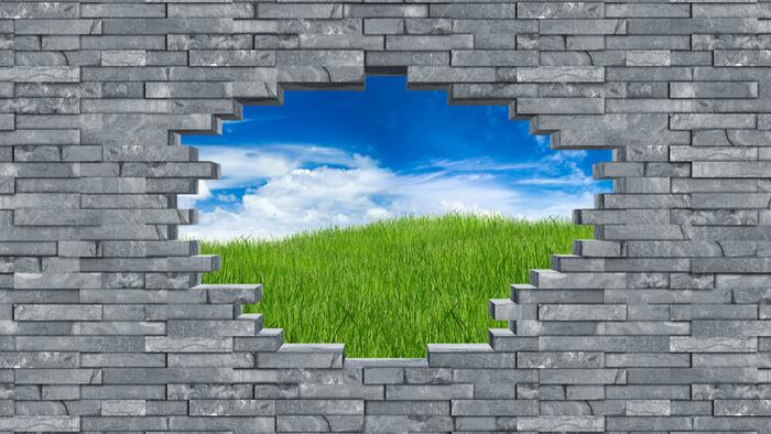 gray slate stone rock wall with breakthrough hole breakout freedom concept in front of green meadow with blue sky background - Image