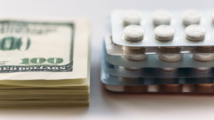 Bundle of money and pack of medication tablets or drug pills, close-up. Expensive health care concept, selective focus