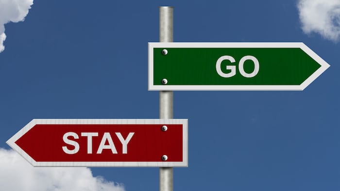 Red and green street signs with blue sky with words Stay and Go, Stay versus Go