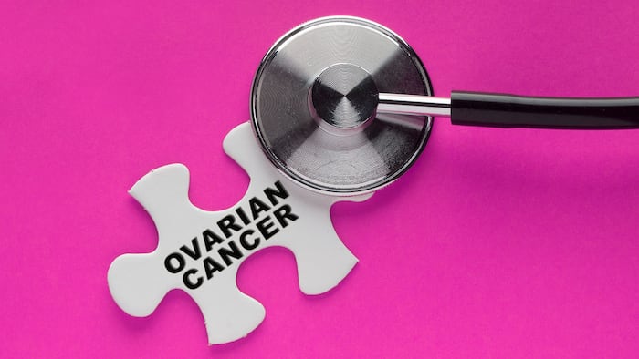 Stethoscope on a white puzzle piece with a written word ovarian cancer on a pink background