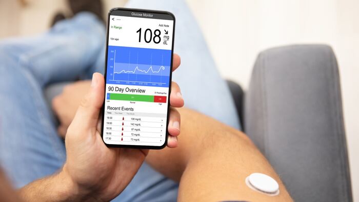 Photo of man holding smartphone with app to track blood sugar open on it.