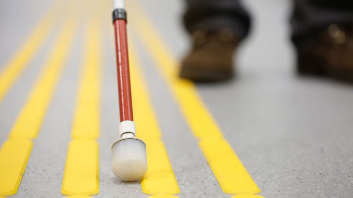 Blind pedestrian walking and detecting markings on tactile paving with textured ground surface indicators for blind and visually impaired.