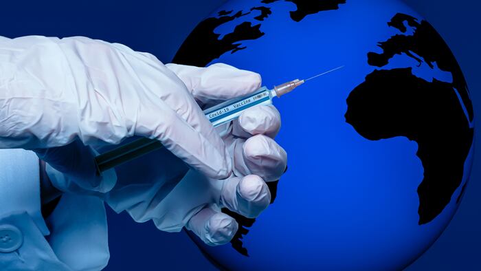 a hand holds a syringe with the inscription covid 19 vaccine in front of globe