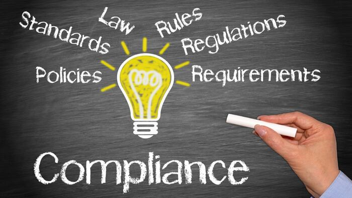 Compliance Business Concept - light bulb with text on blackboard background, female hand with chalk
