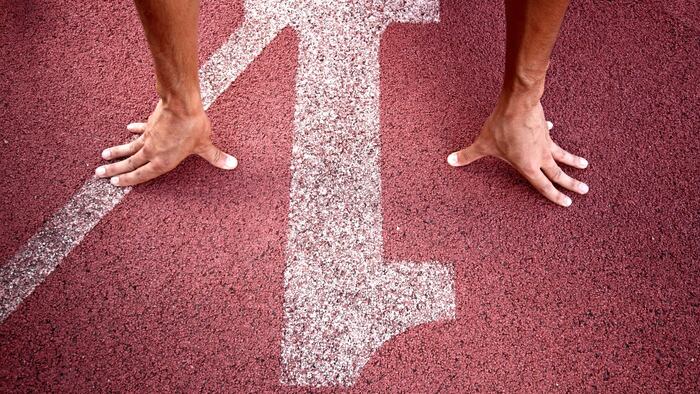 Pair of hands on the red ground of a race track, with a white number one painted on it