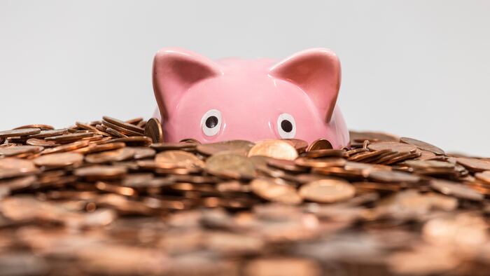 Pink piggy bank drowning in ocean of copper pennies.