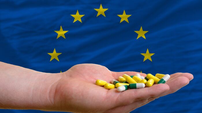 man holding capsules in front of complete wavy national flag of europe symbolizing health, medicine, cure, vitamines and healthy life