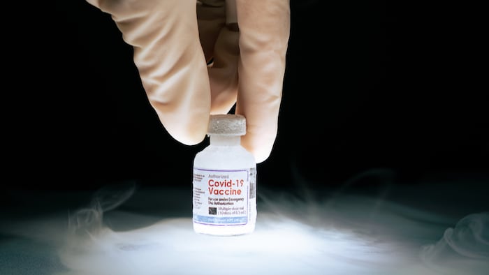 Gloved hand holding mRNA COVID-19 vaccine vial