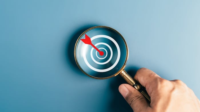 Target with arrow in bullseye, under magnifying glass