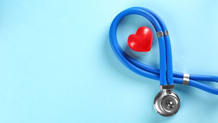Stethoscope and small red heart on color background. Heart attack concept - Image