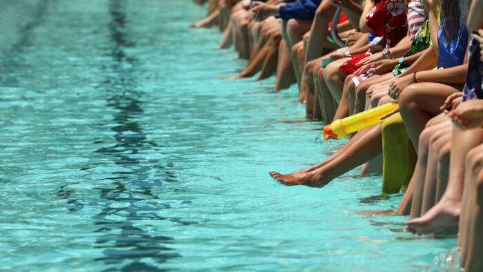 swimming pool with lots of people sitting on side dangling legs in