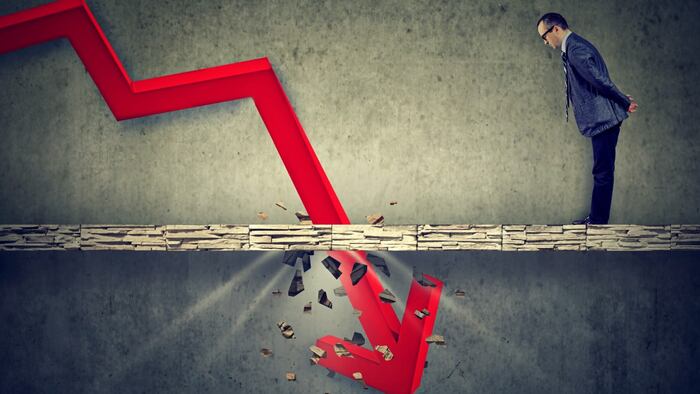 Business man in suit looking at a red arrow pointing downwards, crashing through the ground in front of him