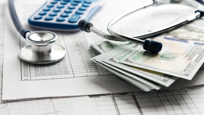 stethescope, calulator, and money on top of helath insurance form