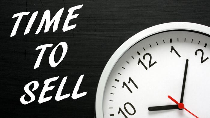 The words Time To Sell in white text on a blackboard next to a modern wall clock as a reminder - Image