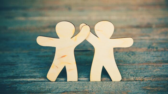 Wooden little men holding hands on wooden boards background. Symbol of friendship, love and teamwork