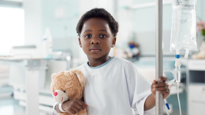 young boy in hospital holding teddy bear and IV pole