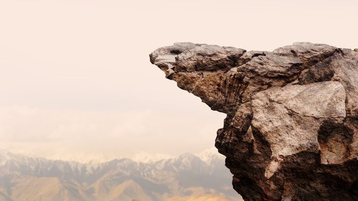 Grey cliff against a light yellow sky, mountains in background