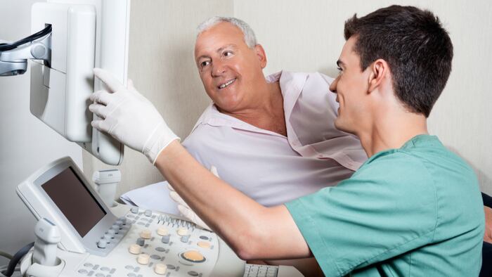 Male technician showing ultrasound machine's monitor to senior patient - Image