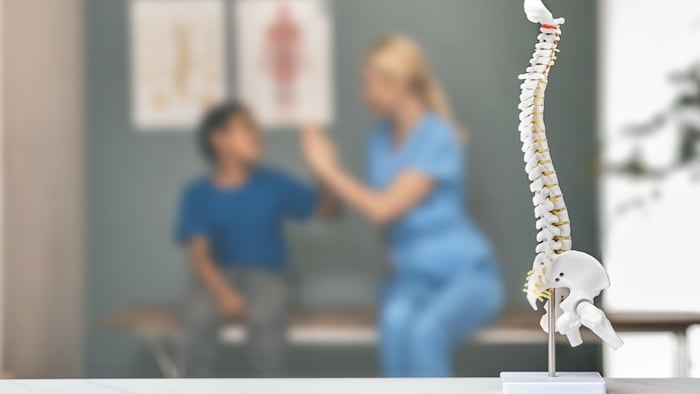 Model of spine in foreground of orthopedist treating a young boy.