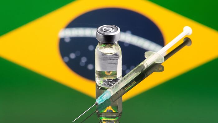 Studio production of syringe, vaccine ampoule and coins, on a blue background, in Brazil