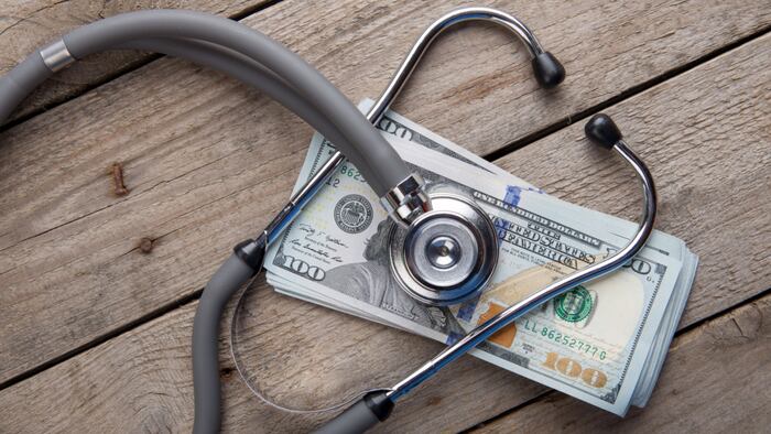 A stethescope overtop of a pile of money on a wooden deck
