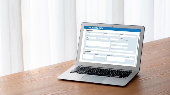A grey laptop sits on a wooden surface. The laptop has a blank, generic form open on the screen.