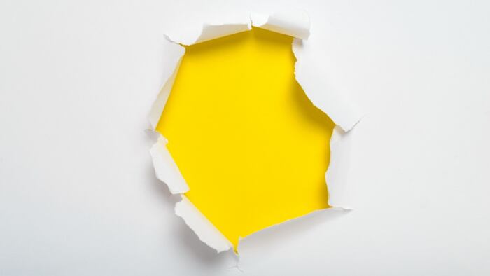 white piece of paper with hole ripped in center revealing yellow background.