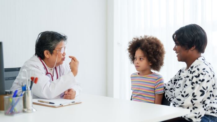 older female doctor talks to young child and parent