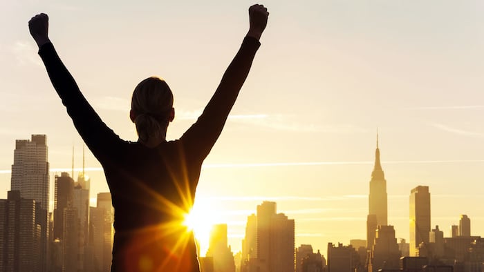 Instagram style filter silhouette of a successful woman or girl arms raised celebrating at sunrise or sunset in front of the New York City Skyline