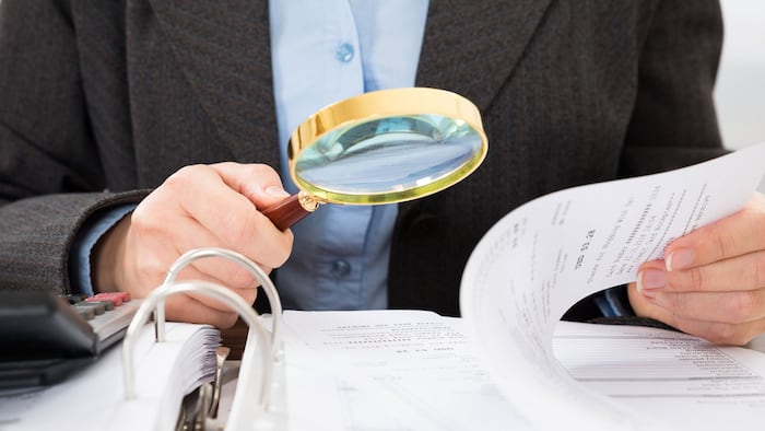 Close-up Of Businessperson Checking Bills With Magnifying Glass