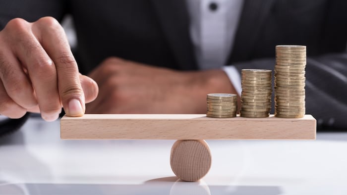 Finger pushing down on scales, balancing piles of coins