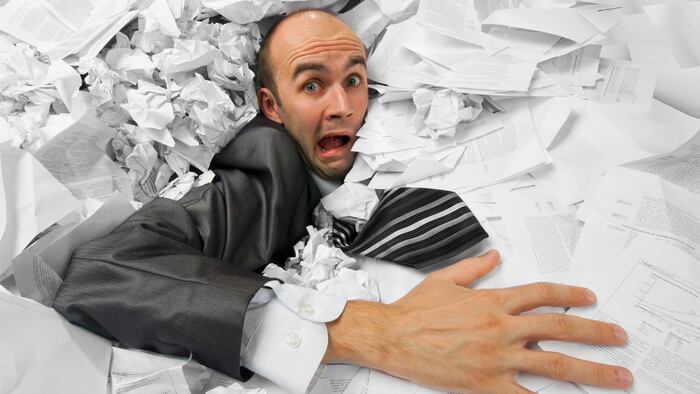 Businessman sinking in heap of documents and asking for help