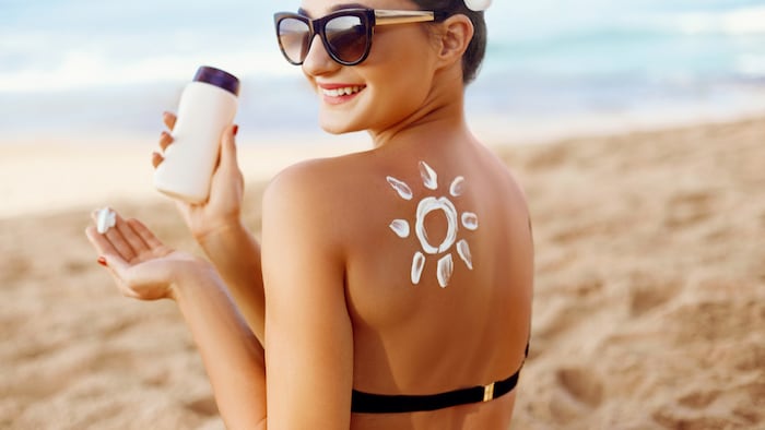 Woman apply Sun cream on tanned back. Skin and Body Care. Sun protection. Portrait of Female in Bikini applying moisturizing sunscreen lotion and Sunblock. Girl Holding Suntan Lotion. - Image