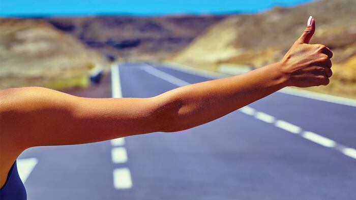 Young caucasian tourist hitchhiking along a road in sunset