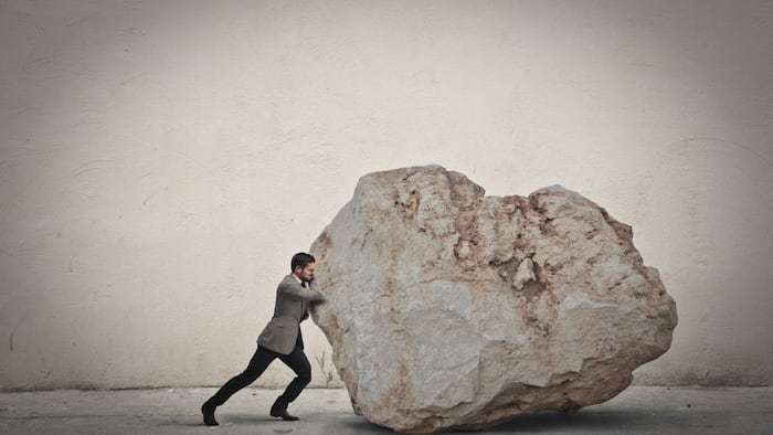 man in suit pushing big boulder